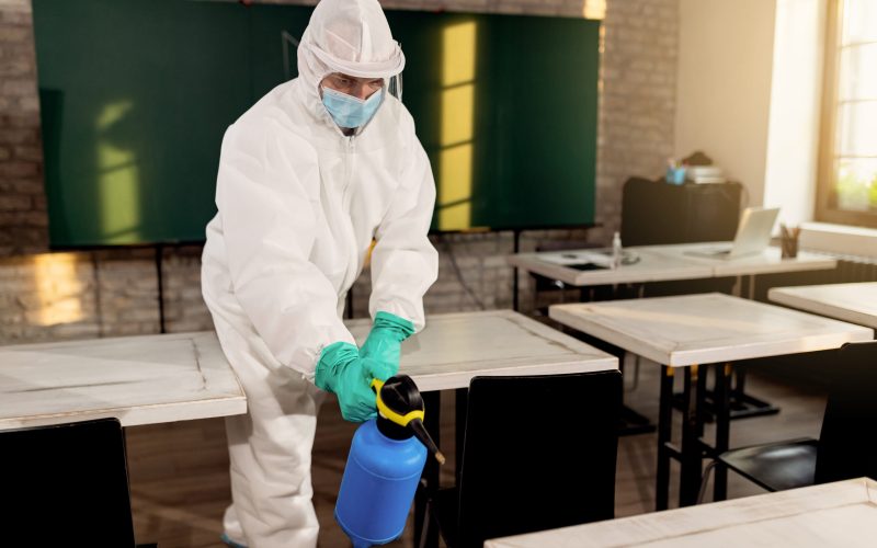 Disinfection worker spraying classroom while preparing school for reopening during coronavirus epidemic.